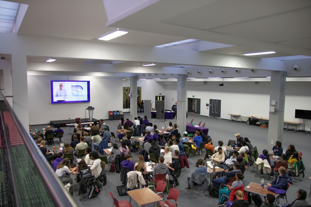 A large group of students sat around tables at a presentation for Personal best